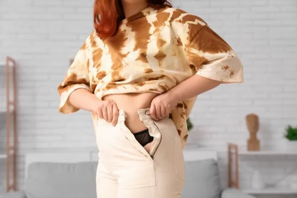 Image of woman trying to do her trousers up after pregnancy weight gain Bibury